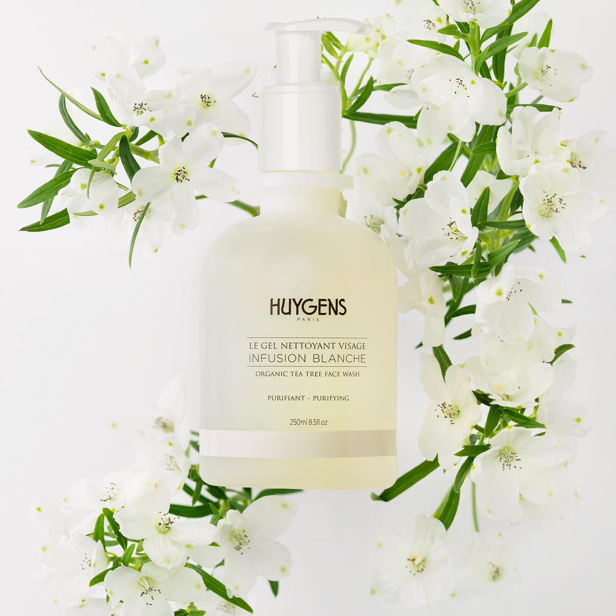 Flacon du gel nettoyant posé parmi des fleurs blanches