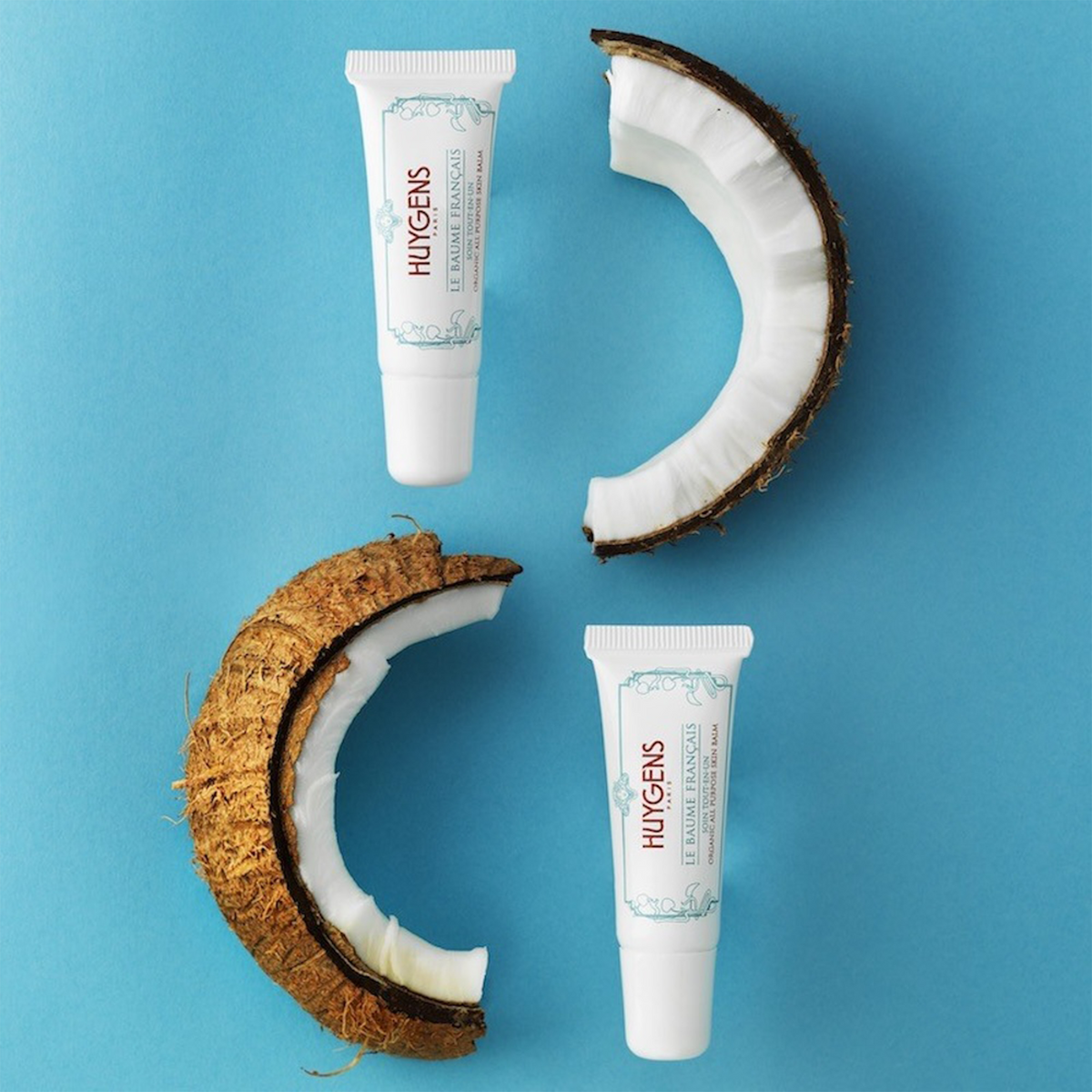 Deux tubes du Baume Français et des moitiés de noix de coco sur fond bleu