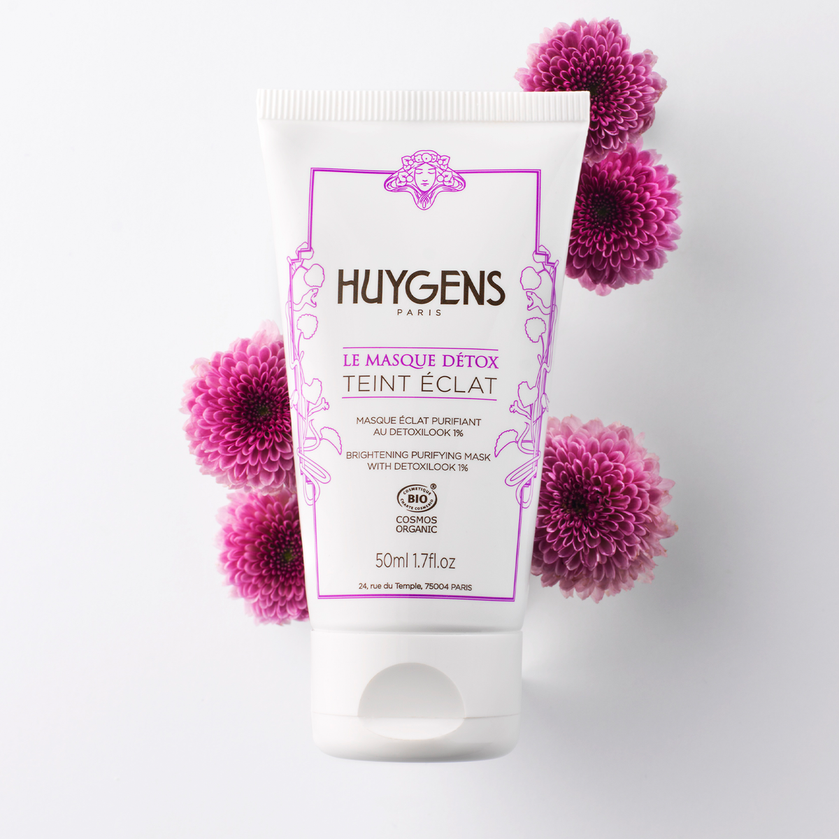 Tube du masque détox posé parmi des chrysanthèmes roses